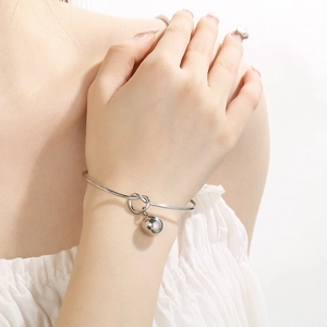 Minimalist silver knotted cuff bracelet with a hollow steel ball pendant on model wrist