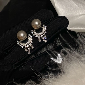 Macro shot of pearl earrings with crescent rhinestones and diamond tassels on black satin