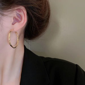 Macro side view of a large gold-plated round hoop earring worn by a model in a black outfit