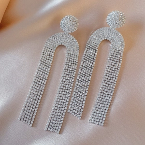 Detailed close-up of long silver rhinestone tassel earrings on elegant champagne silk
