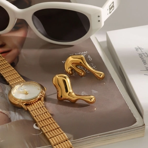 Detail of gold molten metal earrings styled with a watch and sunglasses for fashion
