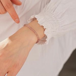 Close-up of pink strawberry quartz beaded bracelet on a white fabric background