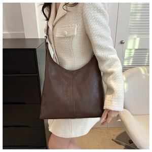 Deep brown PU leather crescent tote bag worn by a model in a minimalist indoor setting