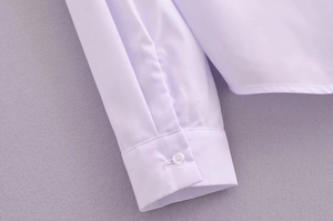Close-up of a white blouse sleeve cuff with a single button and fine fabric texture