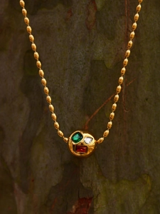 Détail du collier à perles dorées avec pendentif sphérique serti de zircons colorés