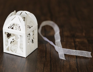 Detail of white laser-cut wedding favor box with romantic silhouettes and thank you text