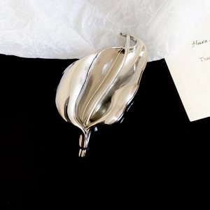 Macro detail of leaf-shaped silver brooch with mirror-polished finish and elegant curves