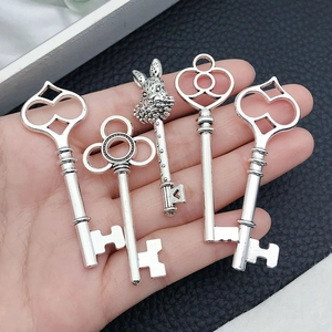 Detail of hand holding five vintage style silver key pendants in different designs