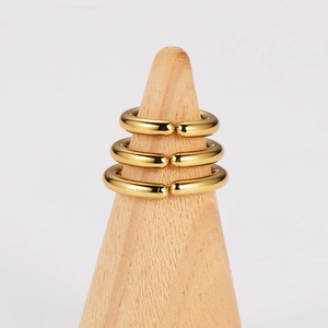 Three gold circular rings displayed on a light wooden cone holder, minimalist style