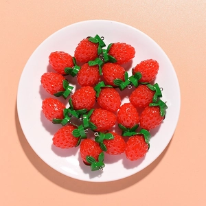 Flat lay of multiple realistic red resin strawberry pendants in a white ceramic dish