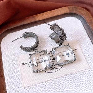 Macro shot of C-shaped metal earrings with square glass pendants on a linen display