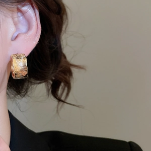 Side view detail of a model wearing wide 18K gold plated textured hoop earrings