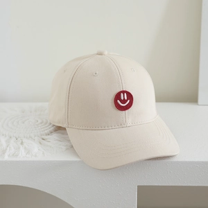 Detail of a beige cotton kids baseball cap featuring a red smiley face patch embroidery
