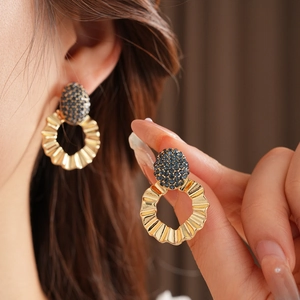 Detailed view of gold hoop earrings with pleated texture and blue pavé crystal studs