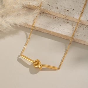 Collier minimaliste à nœud doré sur présentoir en pierre avec roseaux séchés