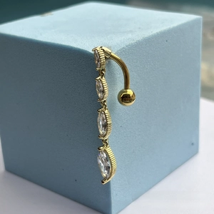 Close-up of golden belly piercing with four marquise-cut zircons on a blue block