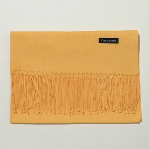 Detail of yellow cashmere scarf showing neat fold, soft texture and branded woven label