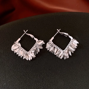 Detail of silver leaf fringe earrings with diamond frames on textured black surface