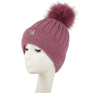 Détail d'un bonnet en tricot rose poudré avec un grand pompon en fourrure et lettre M strass