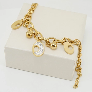 Detail of 18K gold-plated double-layer bracelet with crystal charms on a cream gift box