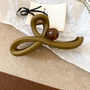Détail d'une pince à cheveux mate vert olive avec une perle décorative aspect marbre