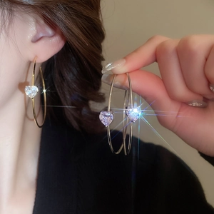 Détail de créoles en forme de C dorées avec zircons en cœur portées par un mannequin