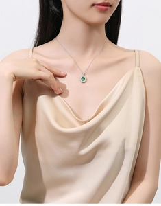 Close-up of oval emerald pendant with white diamond halo on a delicate silver chain