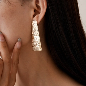 Close-up of golden geometric rectangular earrings with hammered metal texture for women