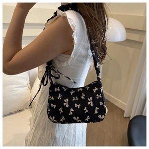 Detail of black crossbody bag with white bow prints and wide shoulder strap