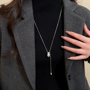 Polished silver teardrop pendant necklace worn over a black turtleneck and grey blazer