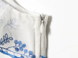 Detail eines verdeckten Reißverschlusses und blauer Blumenstickerei auf weißem Stoff