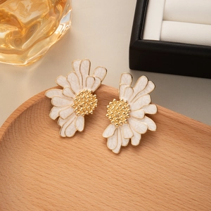 Detail view of white and gold daisy floral earrings on a rustic wooden tray