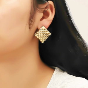 Gros plan d'un mannequin portant des boucles d'oreilles losanges dorées avec texture matelassée