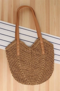 Detail of woven straw tote bag with brown leather straps on striped linen background