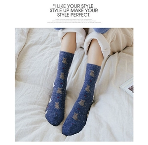 Close-up of navy blue wool knit socks with orange cat patterns and white dots on a bed