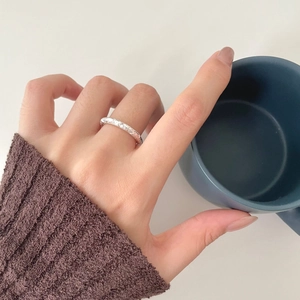 Detailed close-up of a silver irregular textured ring on a model's hand with a blue mug