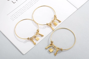 Close-up of golden bangle set featuring star-patterned lock and key charms on white background
