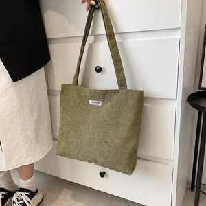 Close-up of green corduroy tote bag with Fashion label hanging on a white drawer