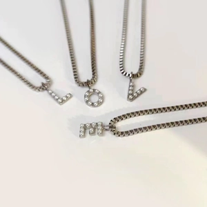 Close-up detail of titanium steel box chain necklace with pearl inlaid letter pendant