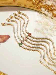 Detail of gold-plated tennis bracelets featuring zirconia flower charms on a mirror surface