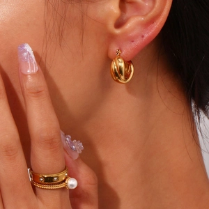 Close-up of gold chunky hoop earrings and layered rings on a female model