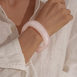 Detailed view of a pink resin bangle with translucent finish worn on a linen sleeve