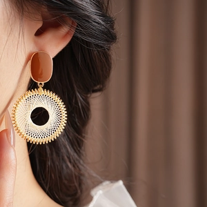 Close-up of earrings featuring golden metal frames and intricate white woven patterns