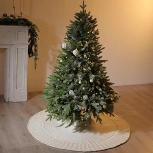 White knitted Christmas tree skirt with intricate woven patterns on a wooden floor