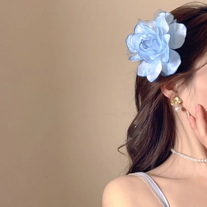 Close-up of a blue fabric rose hair clip worn by a model with elegant pearl jewelry