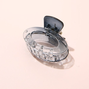 Detail of a transparent grey acetate hair claw clip on a light pink background