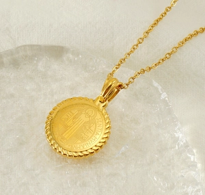 Macro detail of a gold St. Benedict medal pendant on a textured glass display base
