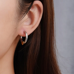 Minimalistische silberne Creolen mit goldenem Herzanhänger am Ohr des Models