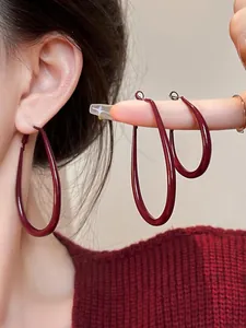 Close-up of deep red teardrop earrings with a glossy finish shown on model
