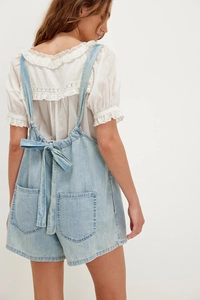 Detail of back bow-tie strap and symmetrical pockets on light blue denim rompers
